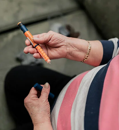 Person holding an orange insulin pen and its blue cap, preparing for injection.