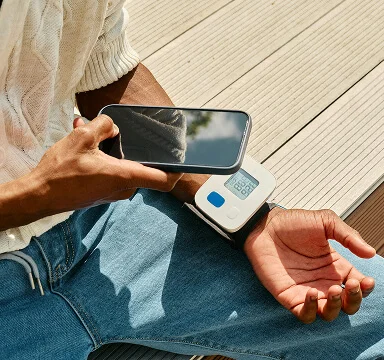 Person measuring blood pressure with a digital monitor on their wrist while holding a smartphone.