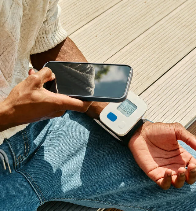 Person wearing a wrist blood pressure monitor while holding a smartphone.