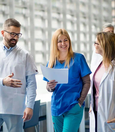Smiling medical professionals in scrubs and white coats walking and talking in a bright hospital corridor.