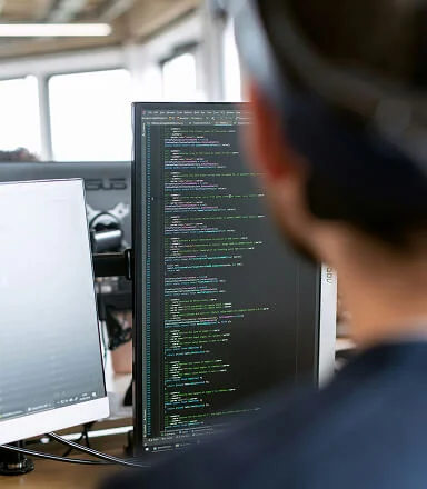 Person viewing computer screen filled with lines of code in a modern office setting.