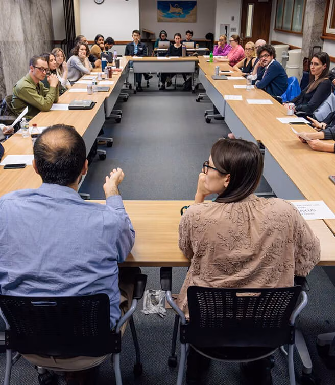 A diverse group of people seated around a large U-shaped conference table engaged in a meeting or discussion in a professional setting.