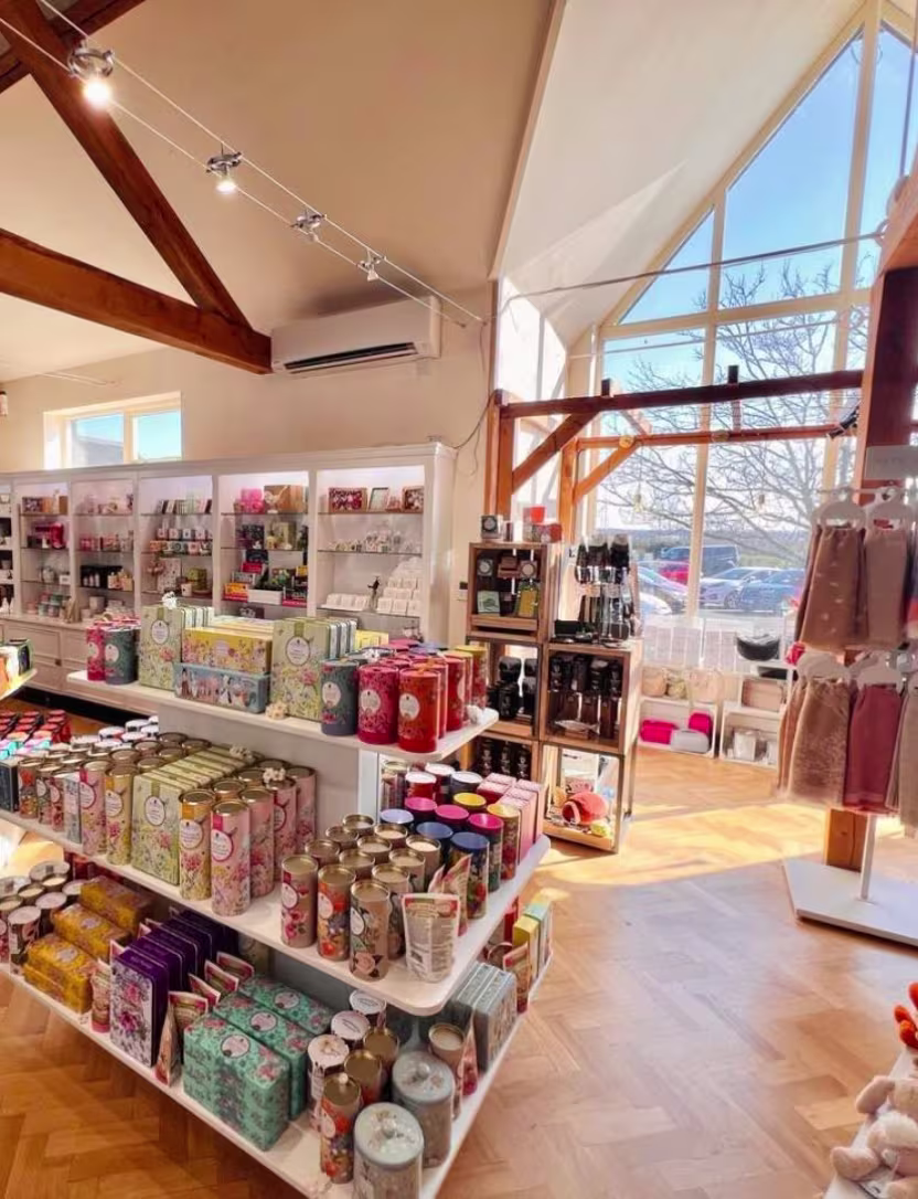 Bright gift shop interior with shelves displaying candles, toiletries, and accessories by large windows.