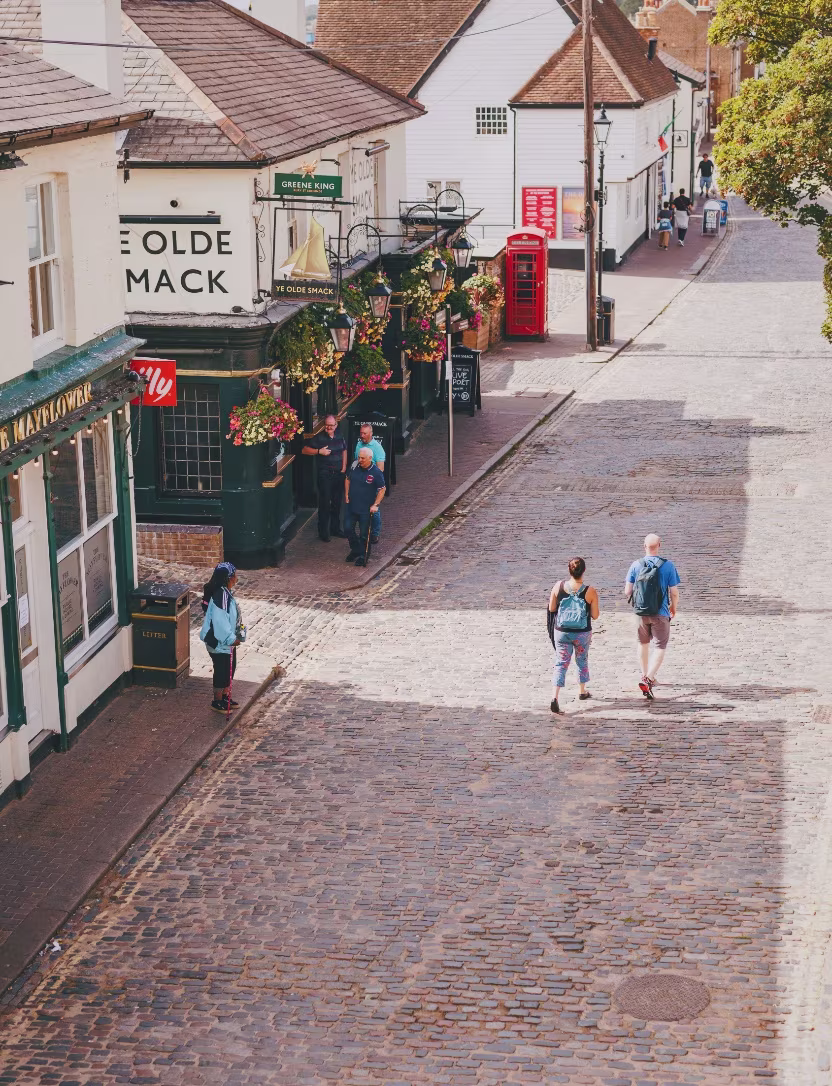 Cobblestone street with pedestrians, old English pub with hanging flowers, and a red telephone box.
