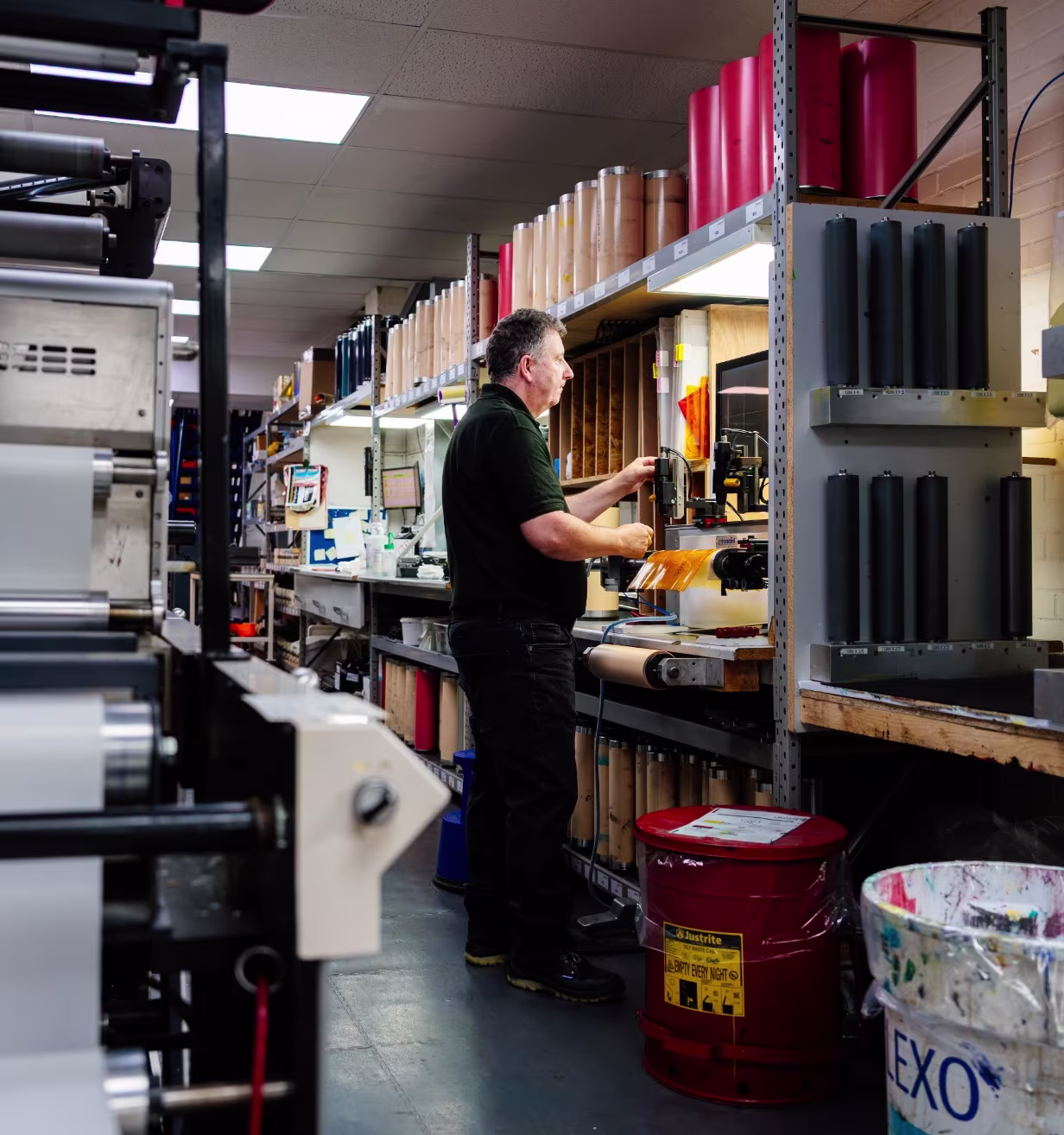 Man working with printing materials and machinery in a warehouse or workshop setting.