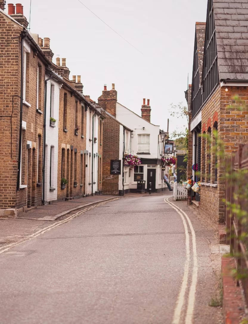 Quiet street lined with brick and white houses, adorned with flower baskets on a cloudy day.