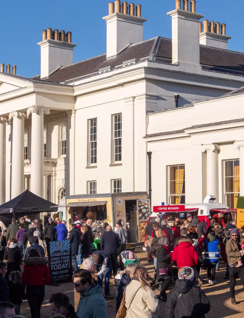 Crowd gathering at street food market outside a large white building under clear blue sky.