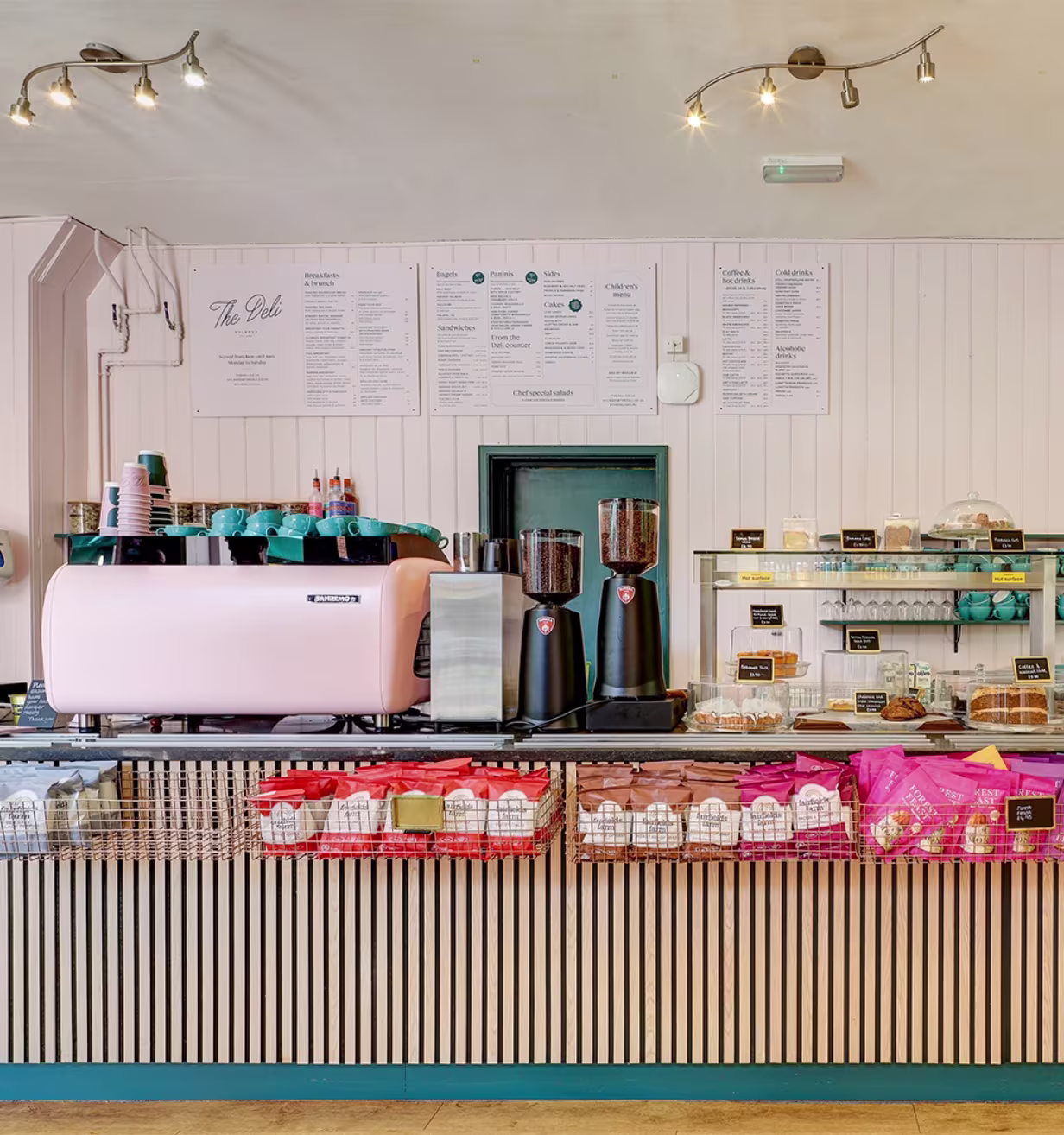 Counter with coffee machine, grinders, snacks, and cakes in a bright modern deli café.
