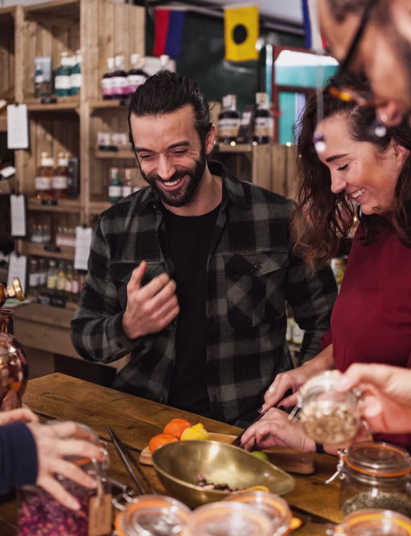 Smiling people gathered around a wooden table with jars and fruit in a cozy store setting.