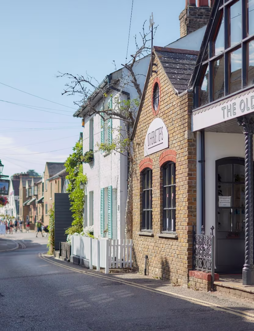 Quiet street with brick building and white houses with shutters in a sunny village scene.