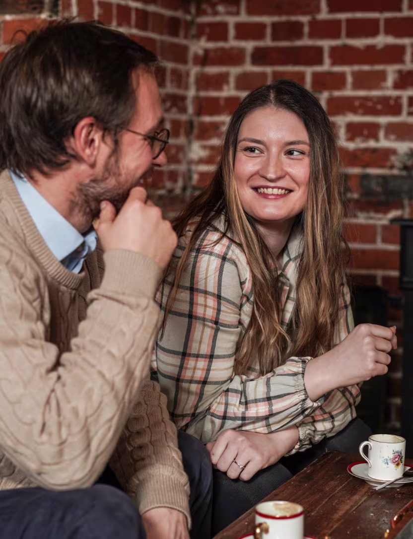 Smiling woman and man talking in a cozy brick-walled café with cups of coffee on the table.
