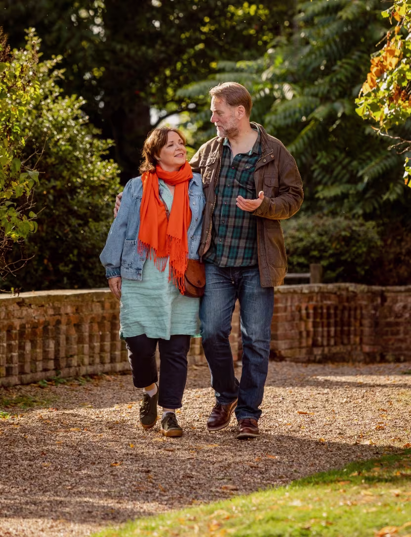 Middle-aged couple walking arm in arm on a path surrounded by autumn trees and foliage.