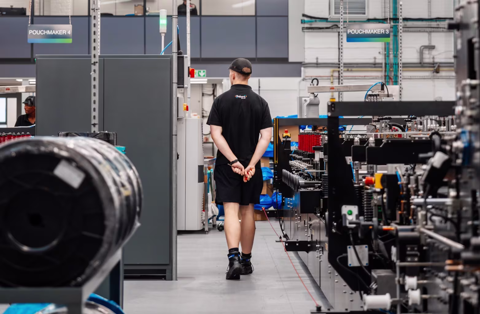 Person in black uniform walking through a factory aisle with large industrial machines around.