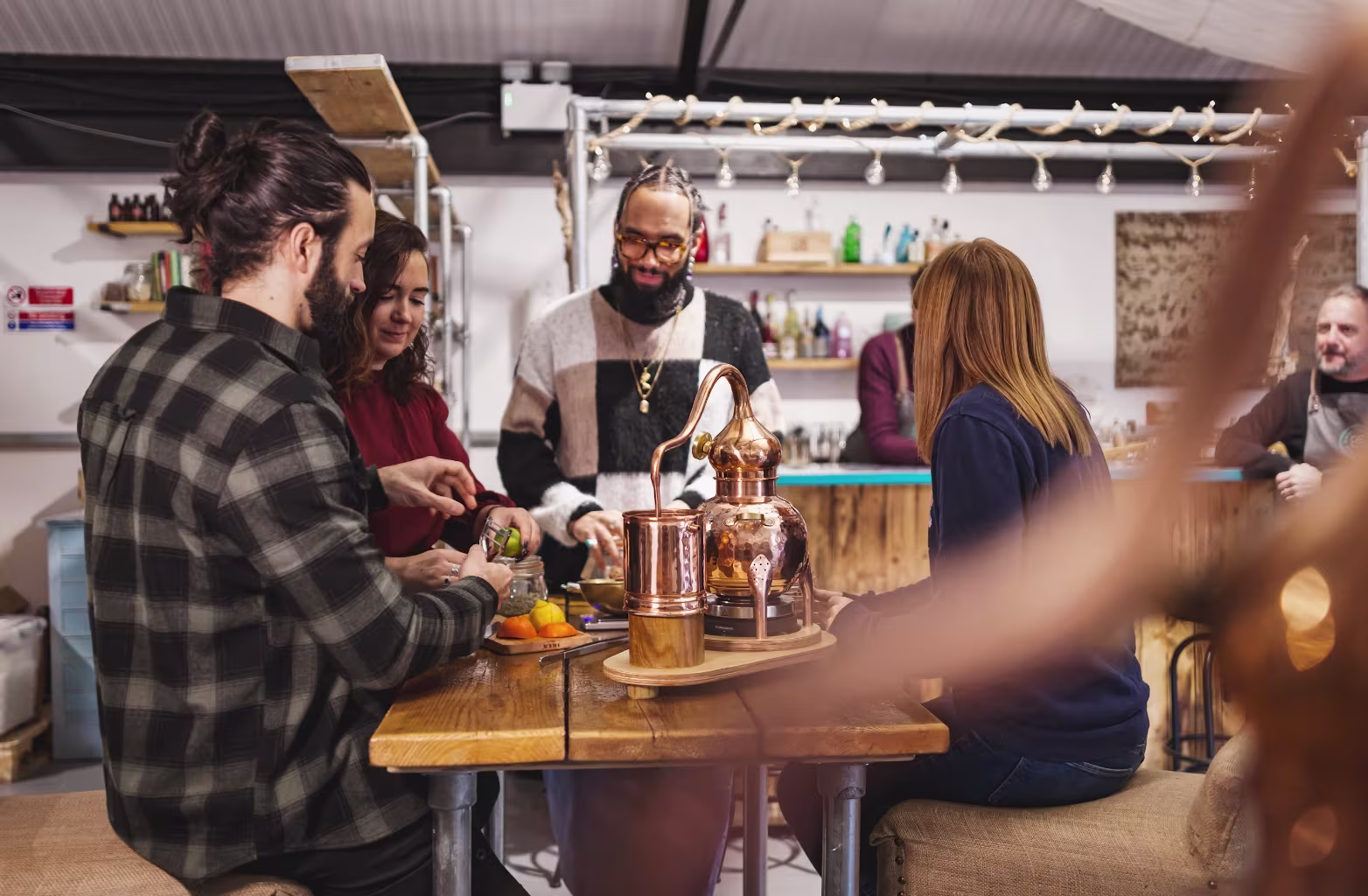 Four people around a wooden table preparing food or drinks in a rustic kitchen or bar setting.