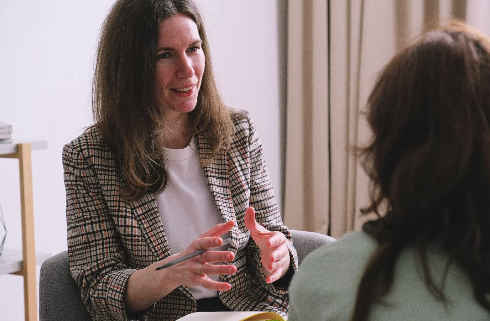 Woman explaining something with hand gestures while sitting and talking to another person.
