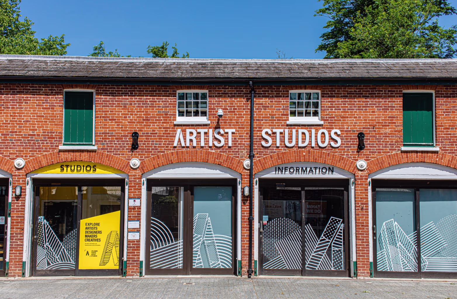Red brick building with green doors and windows, labelled Artist Studios and Information with graphic designs on glass.
