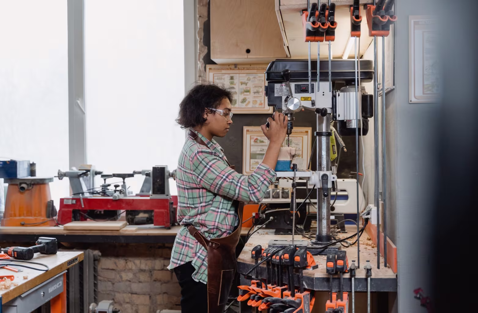 Person wearing safety glasses using a drill press machine in a woodworking workshop.