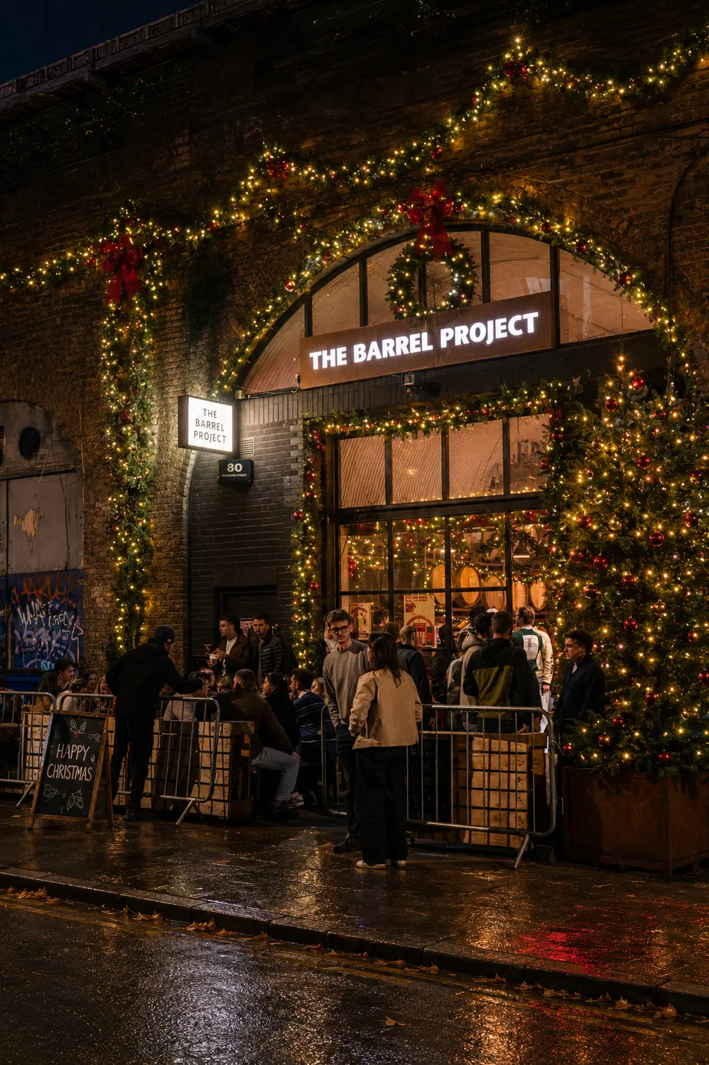 Night view of The Barrel Project bar entrance decorated with Christmas lights and a tree outside.