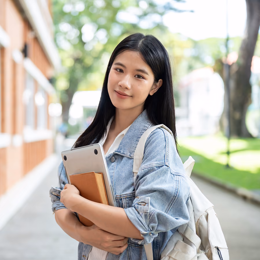 A college student holding a laptop on campus, requiring a college accommodations evaluation for learning support