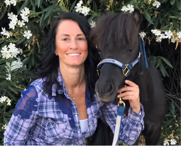 Founder Andrea Torzon smiling next to a miniature horse at Twinkle Twinkle Little Farm