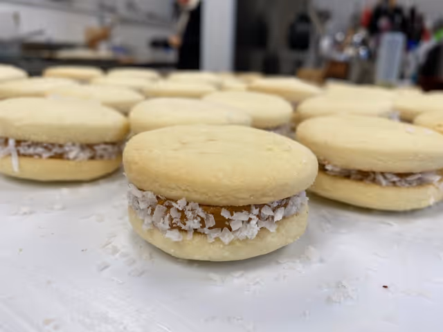 Close-up of alfajores cookies with dulce de leche and coconut flakes on a white surface.