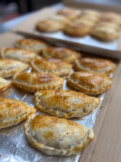 Close-up of multiple freshly baked golden brown empanadas arranged on foil in a cardboard box.