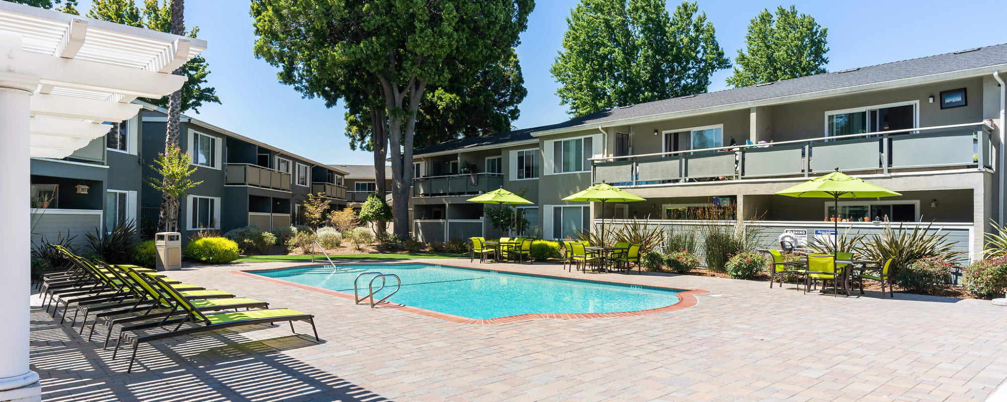 Swimming pool with lounge chairs with umbrellas and tables and view of exterior