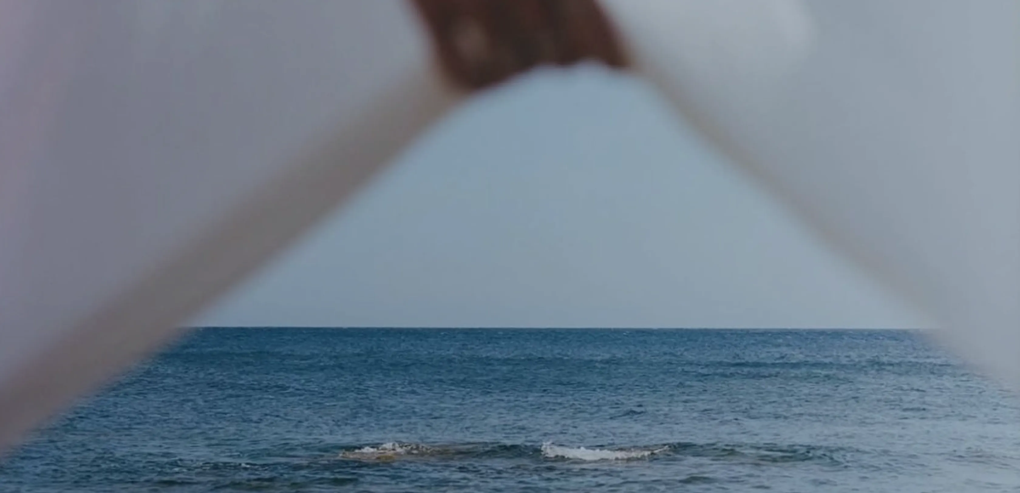 View of a calm ocean horizon framed by blurred white shapes forming a triangle in foreground.