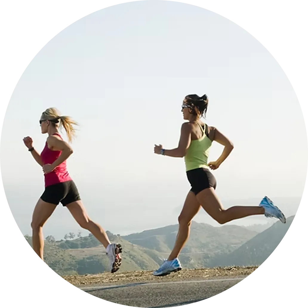 Two women running on a mountain road with hills and sky in the background.