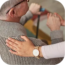Hand in a watch gently resting on shoulder of an older person wearing a knitted sweater.