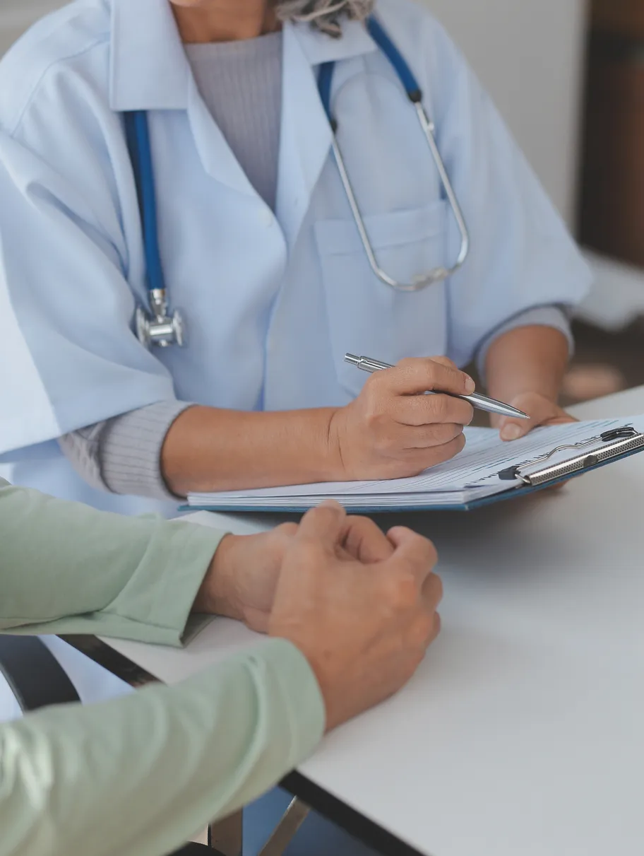 Doctor in white coat with stethoscope reviews forms with a patient at a desk.