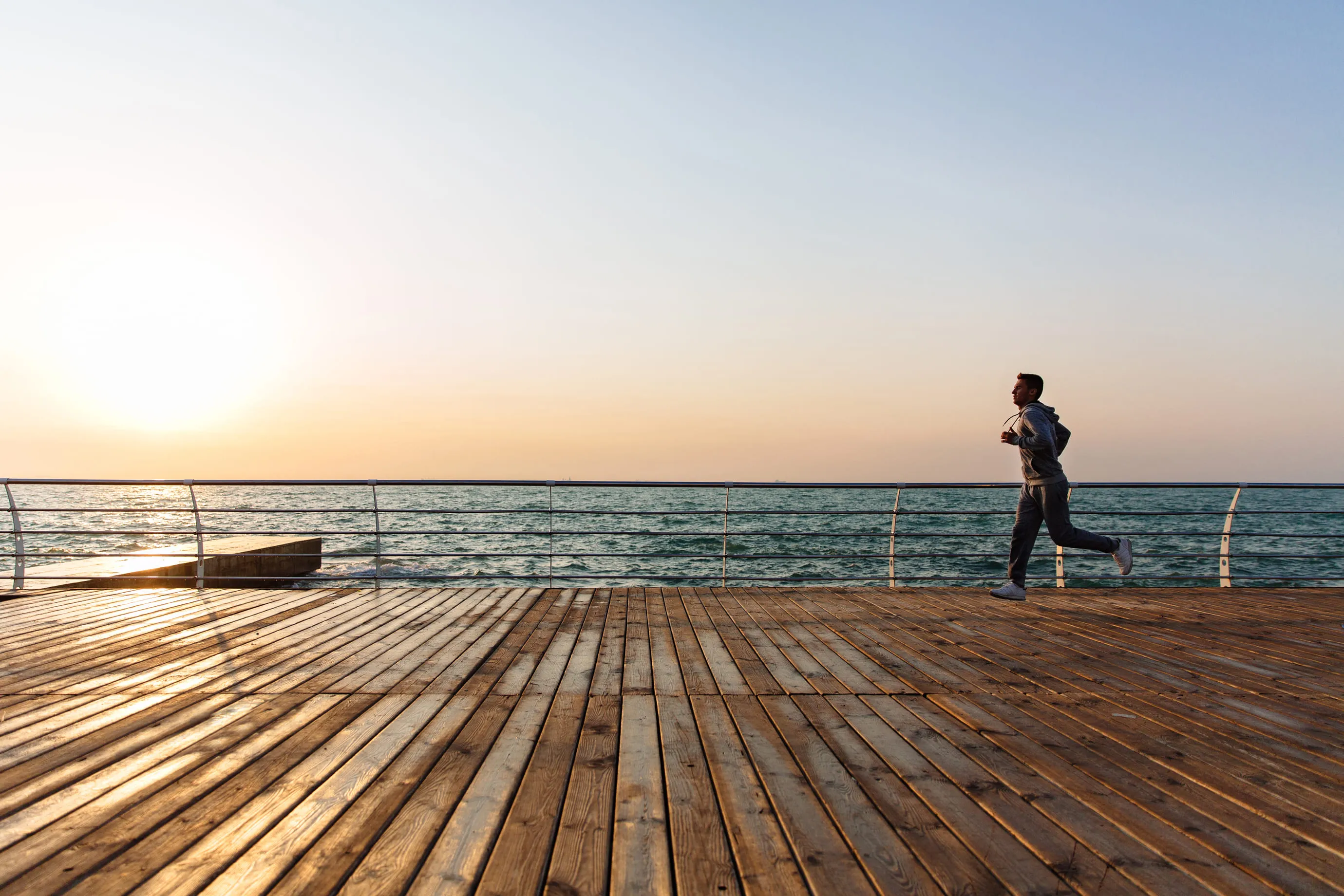 Man jogging on a wooden pier near the sea during a peaceful sunset.