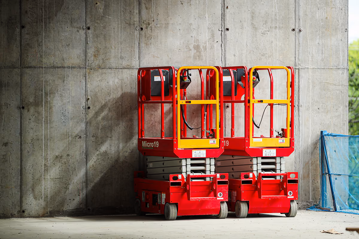 Two red scissor lifts with yellow safety rails parked inside a concrete-walled building.