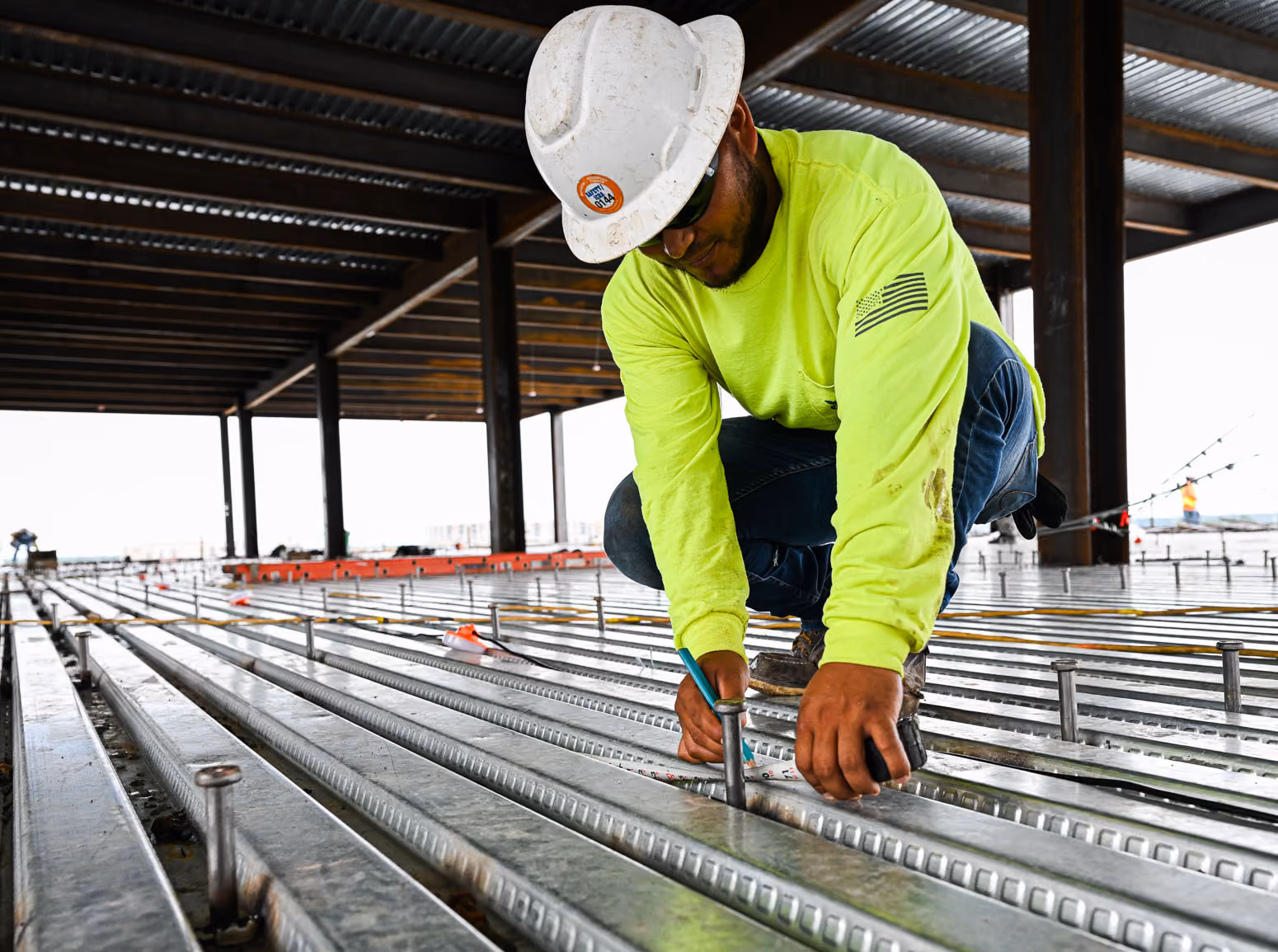 Construction worker in neon shirt and hard hat marking metal beams on a building site.