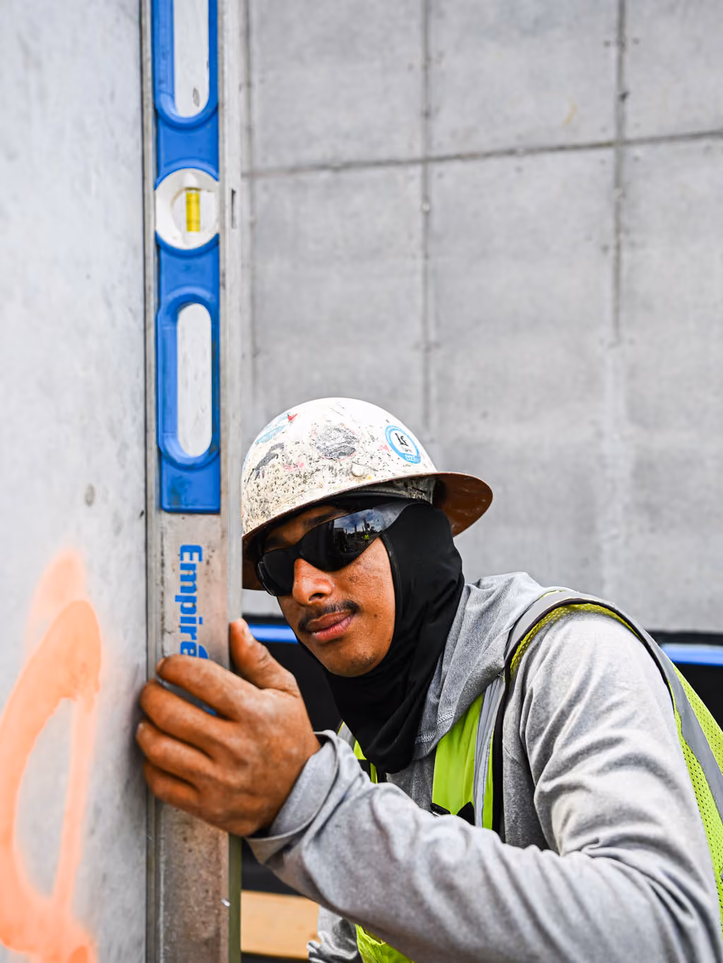 Construction worker wearing safety gear using a level against a concrete wall.