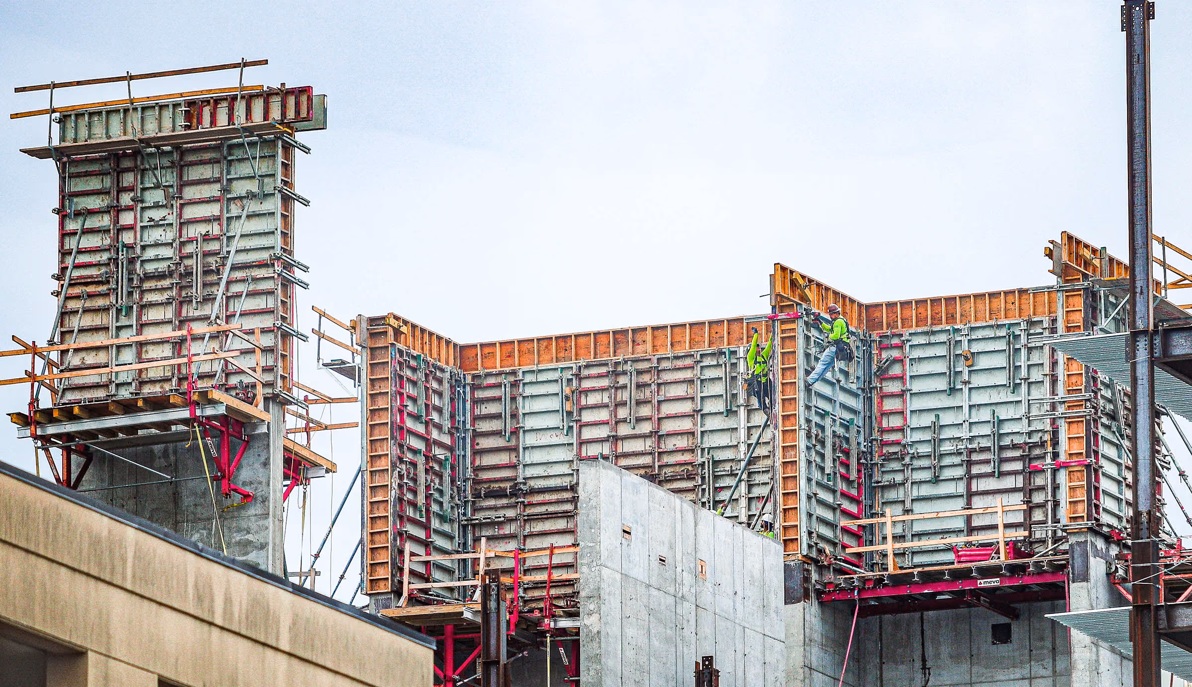 Two construction workers in safety gear working on a large concrete building framework.