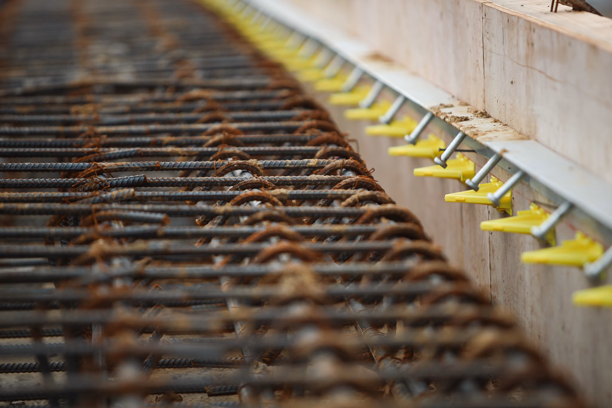 Close-up of rusted steel rebar grid next to concrete and yellow spacer clips in construction.