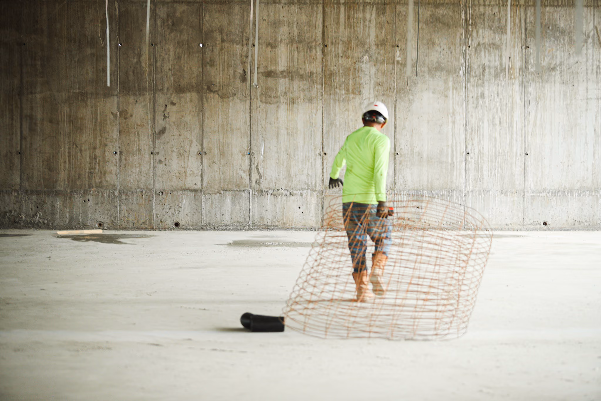 Construction worker in a neon shirt and helmet walking inside an unfinished concrete building.