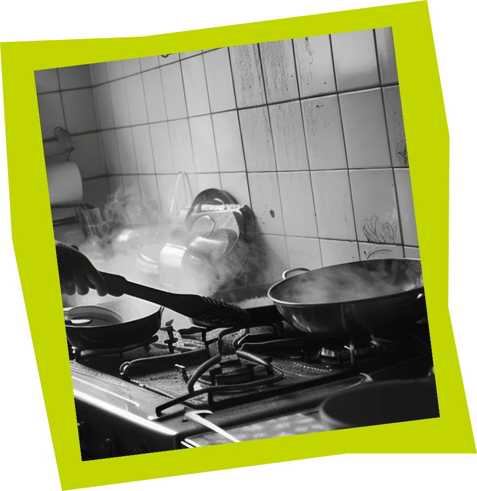 Black and white photo of a hand stirring food in a steaming frying pan on a gas stove.