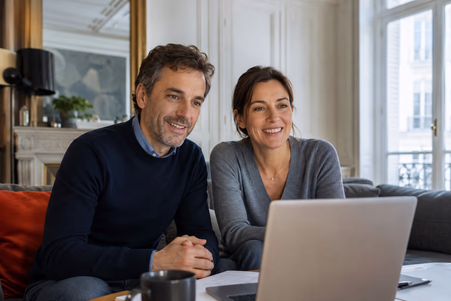 Un couple assis sur un canapé souriant en regardant un ordinateur portable devant eux.