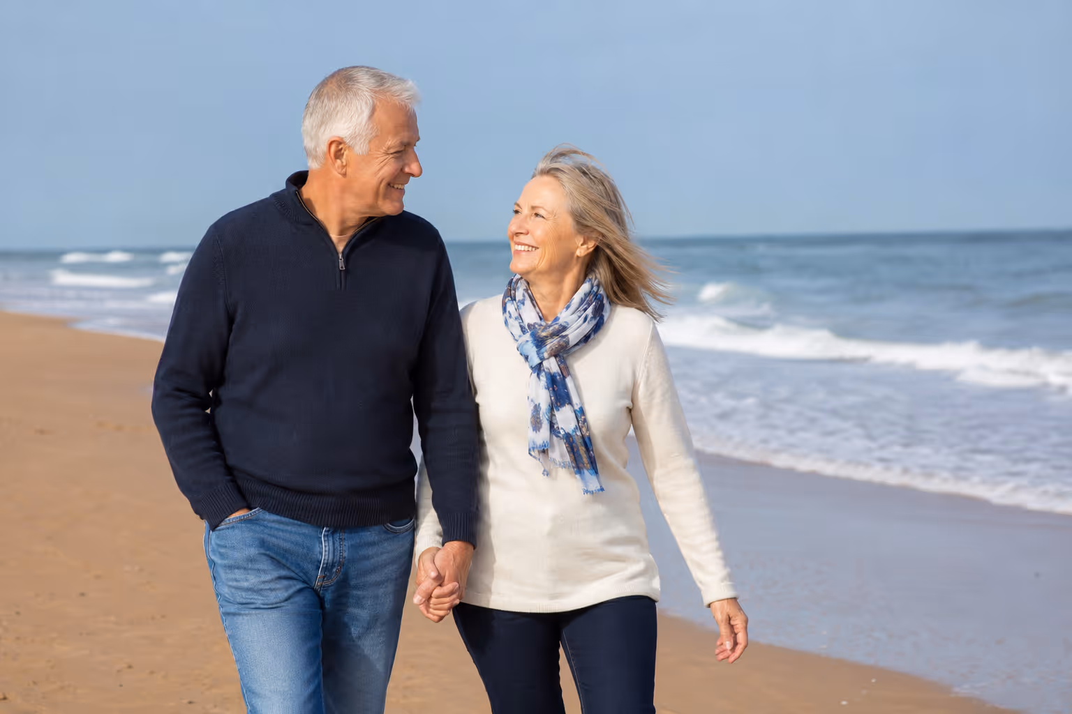 Couple senior marchant main dans la main sur une plage par temps clair.