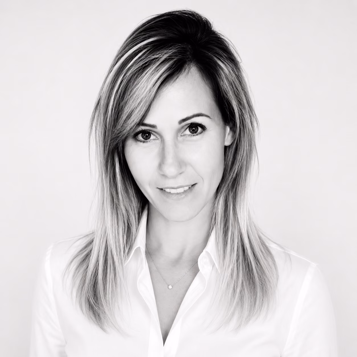 Portrait en noir et blanc d'une femme souriante aux cheveux longs et chemise blanche.
