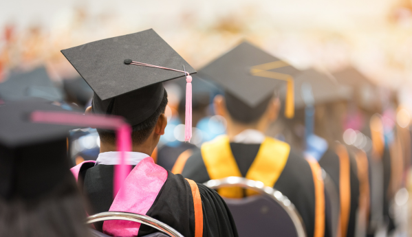 Graduates wearing caps and gowns with colorful stoles seated facing forward at a ceremony.
