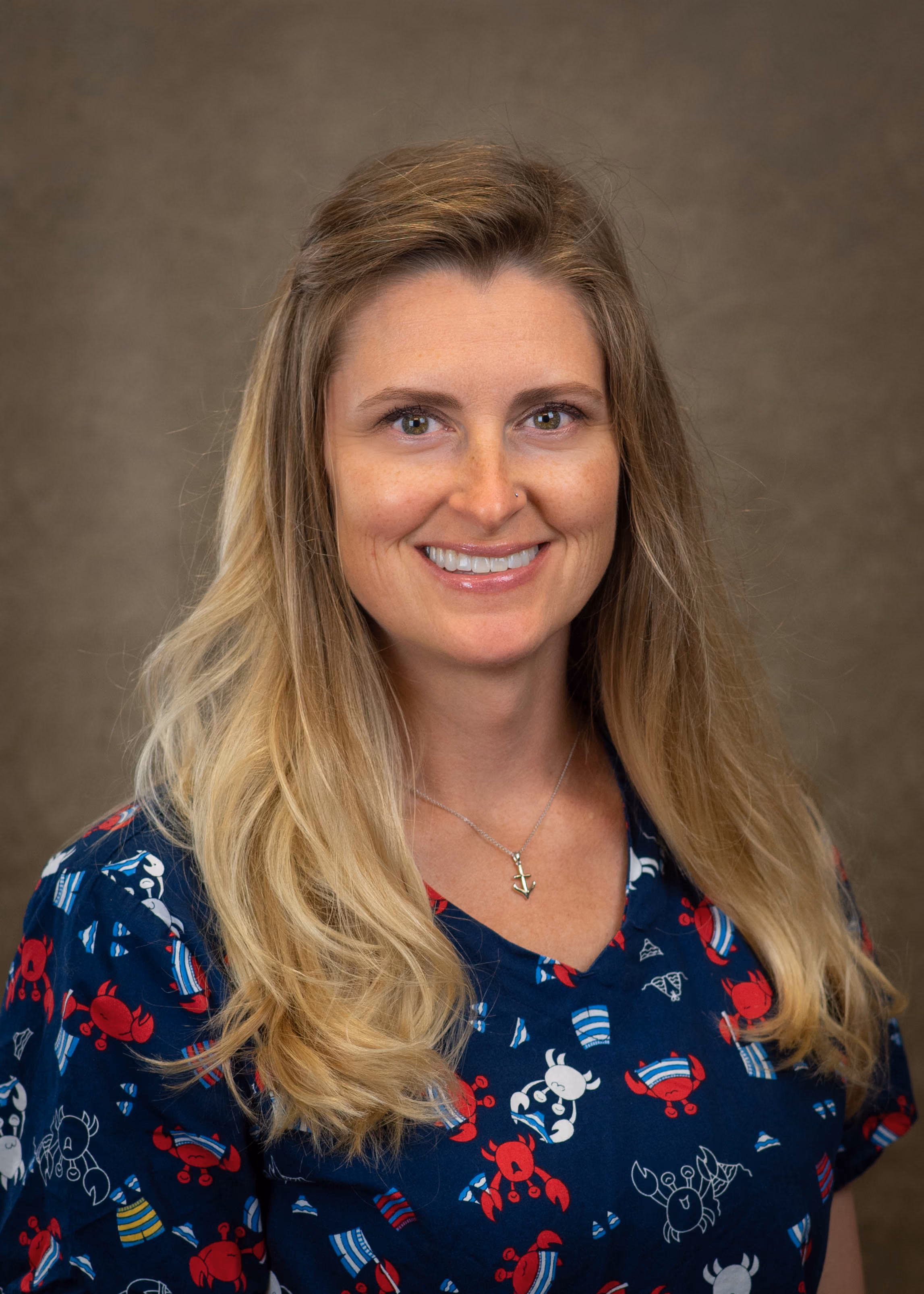 Smiling woman with long blonde hair wearing a blue shirt with red and white crab patterns and an anchor necklace.