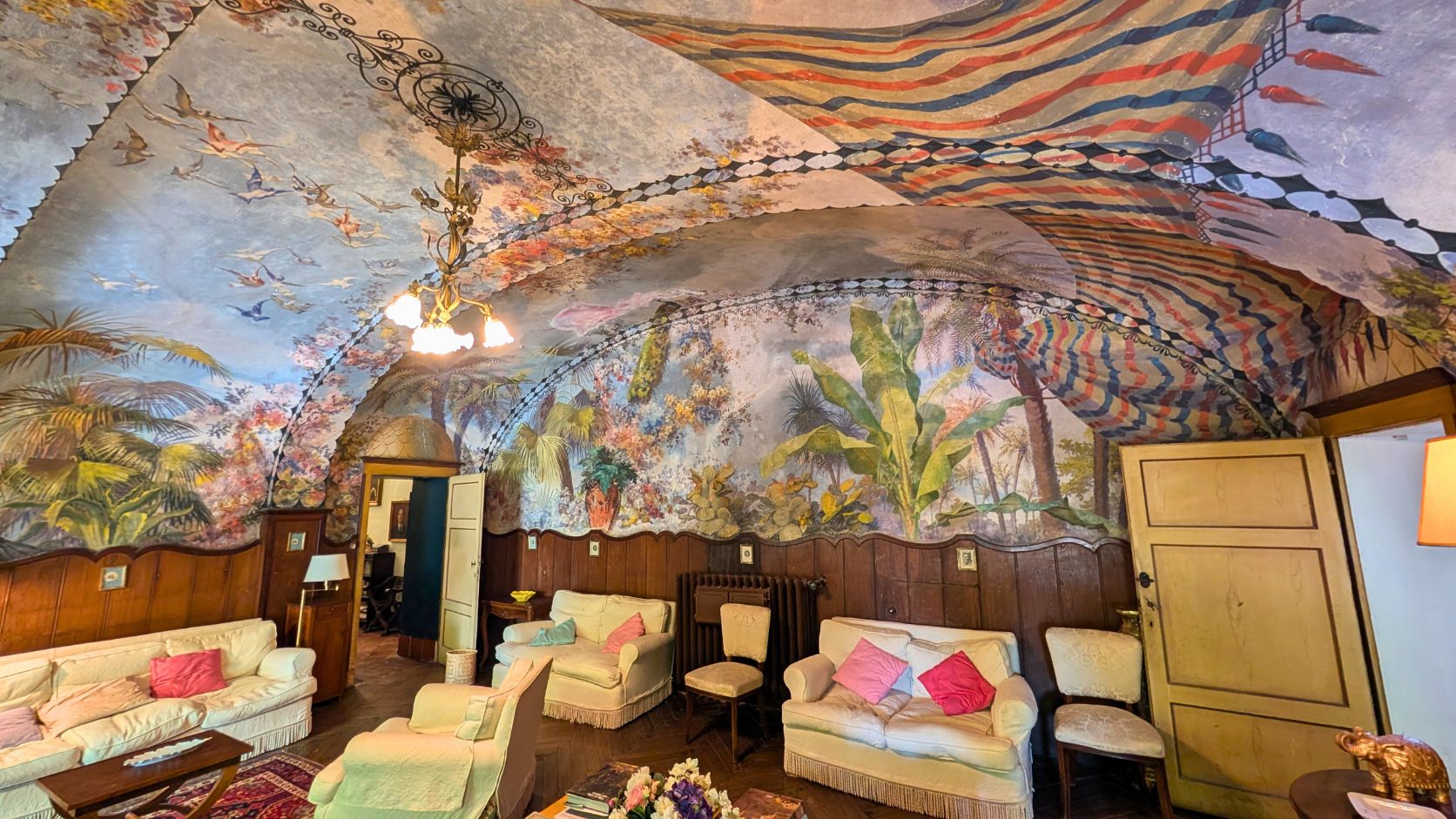Room with a painted arched ceiling featuring birds, plants, and colorful stripes, plus sofas and chairs, Castello Higo, Tuscany.