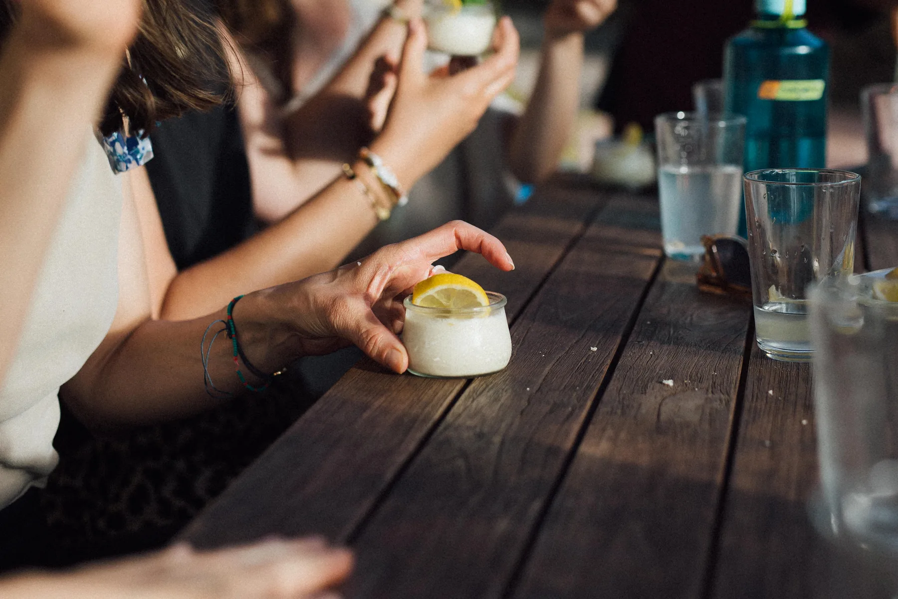 A person holding a small dessert topped with a lemon slice on a wooden table with others in the background, Castello Higo, Tuscany.