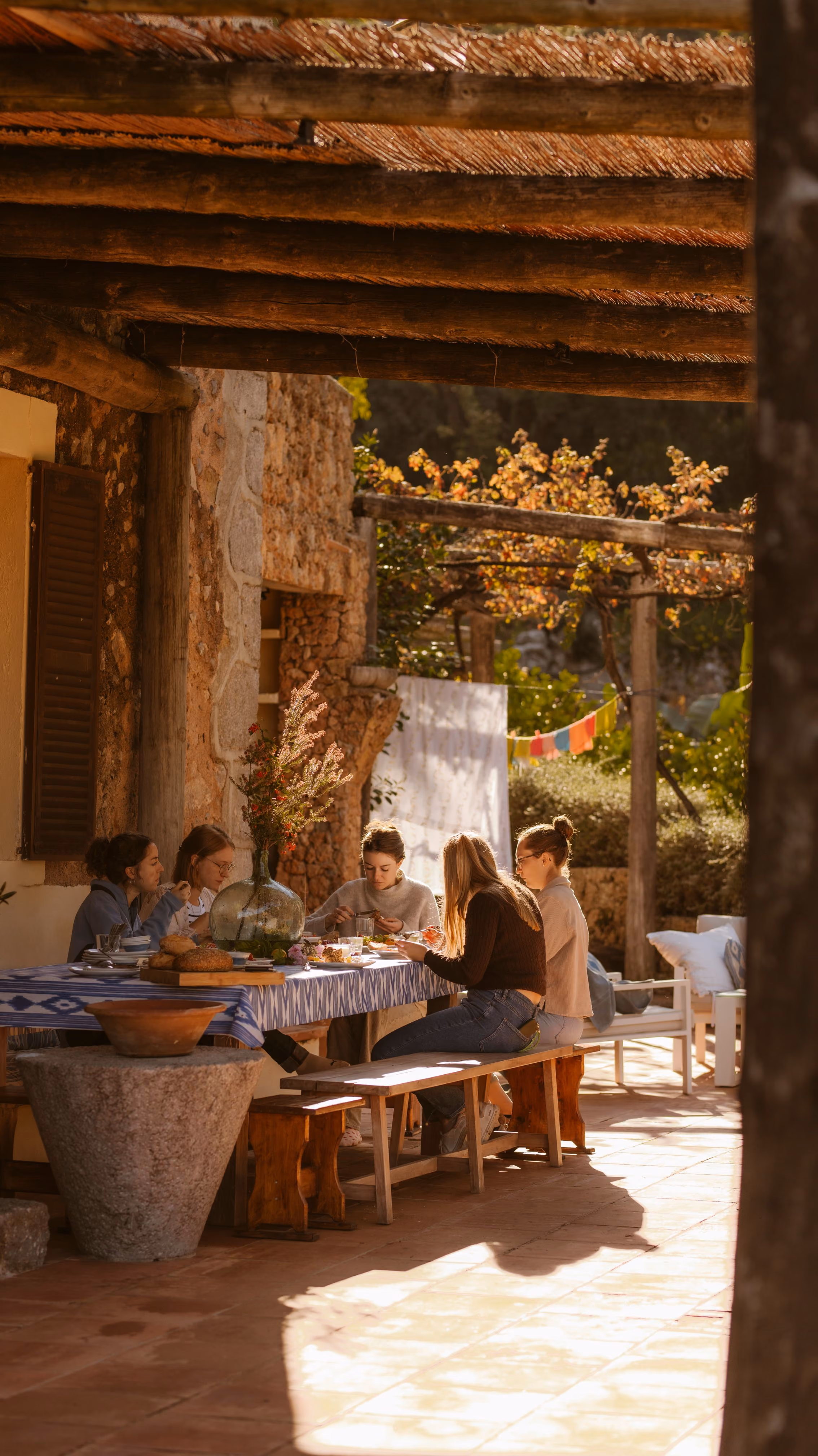 Group of women enjoying an outdoor brunch under a vine-covered pergola at Finca Higo, Mallorca.