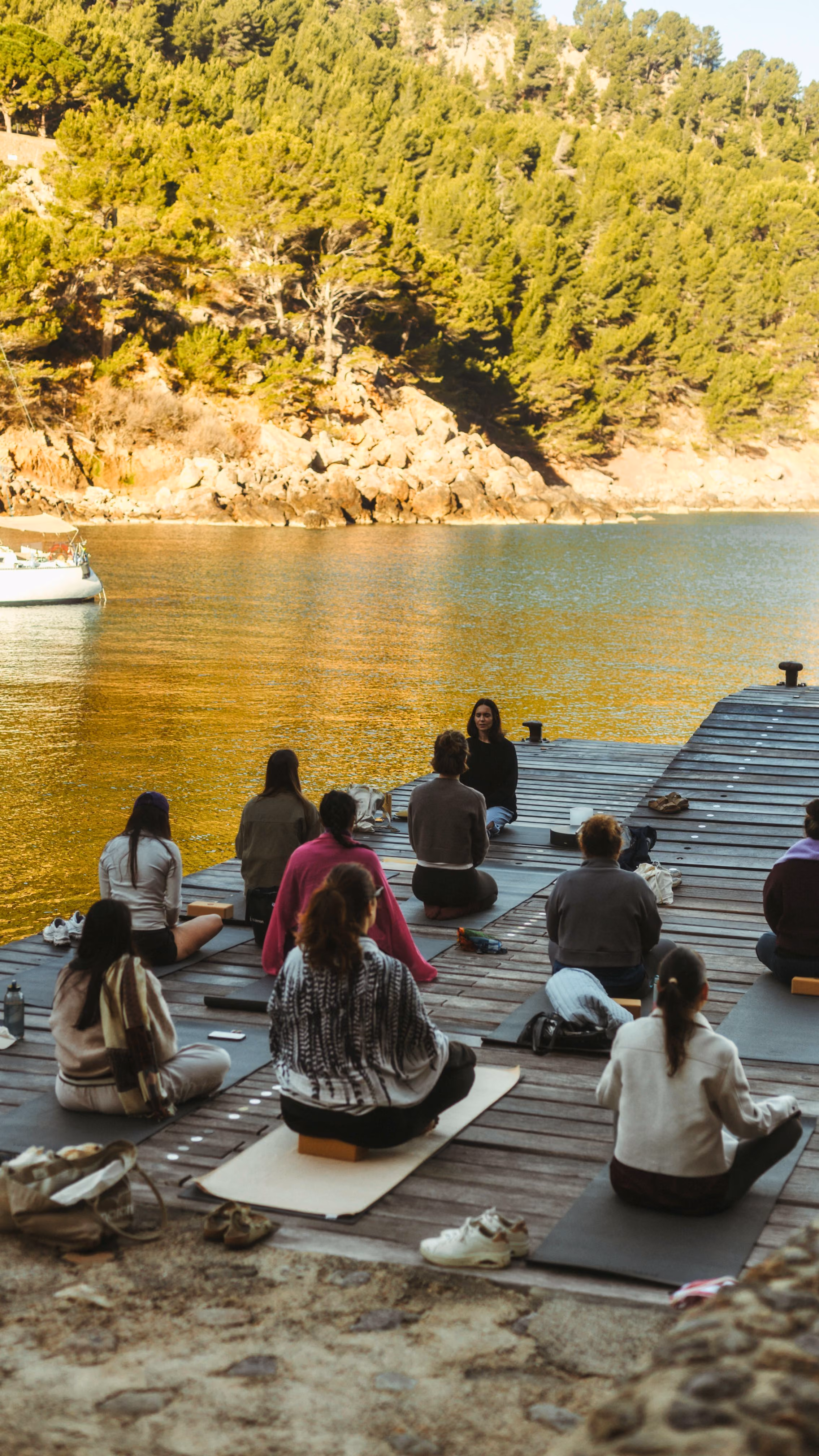 Group meditating on a wooden dock at golden hour, overlooking the water near Finca Higo, Mallorca.