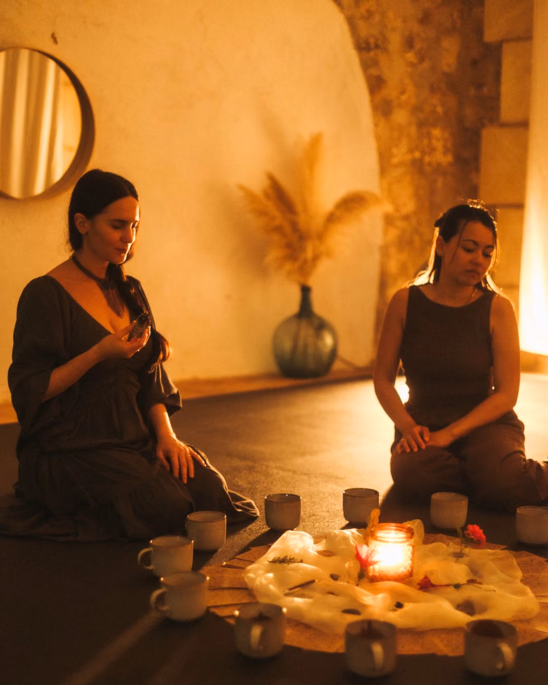 Two women sitting cross-legged near a candlelit arrangement inside the Finca Higo yoga studio, Mallorca.