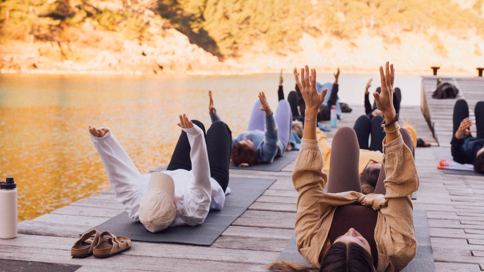 Group of people lying on yoga mats on a dock by the water on the coastline of Mallorca.